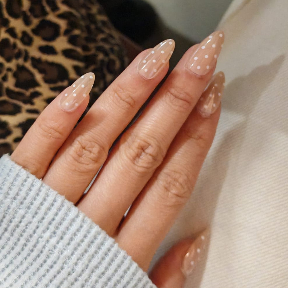 Press-on nails, faux onlges. Main avec manucure nude en forme amande à pois blancs. 