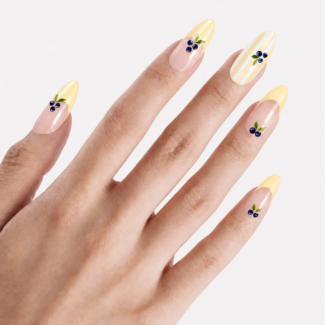 Faux ongles press-on Mirtillo portés sur la main, manucure longue amande nude avec French jaune beurre et myrtilles 3D