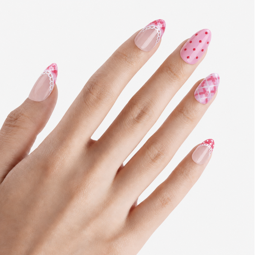 Faux ongles press-on Rosalie portés sur la main, manucure rose amande avec motifs vichy, pois et dentelle