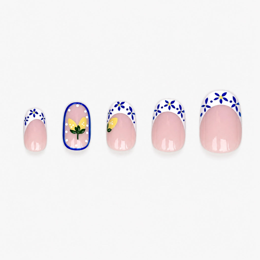 Faux ongles press-on Maiolica courts ronds avec base nude, motifs bleu profond et blanc façon céramique italienne, citrons jaunes et French revisitée