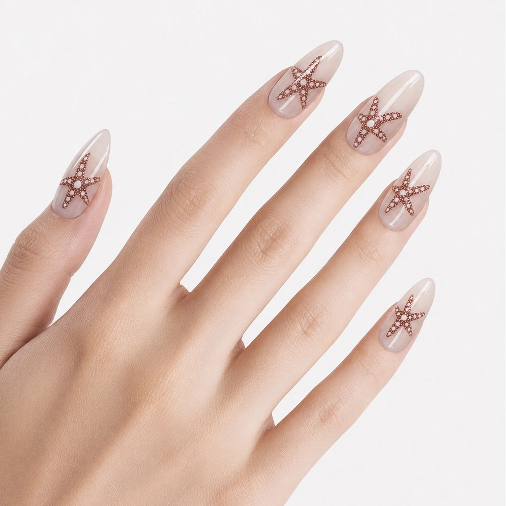 Faux ongles press-on Stella Marina portés sur la main, manucure longue amande blanc lacté avec étoiles de mer dorées et esprit bord de mer