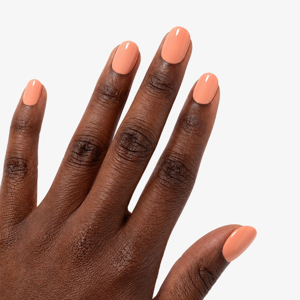 Manucure Nude Abricot portée sur la main teinte fonce, faux ongles press-on courts arrondis nude pêche brillant effet naturel