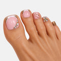 Pédicure press-on Feu d’Or portée aux pieds avec base nude rosée, strass lumineux et détails dorés en sandales. Par SOIMEA Paris