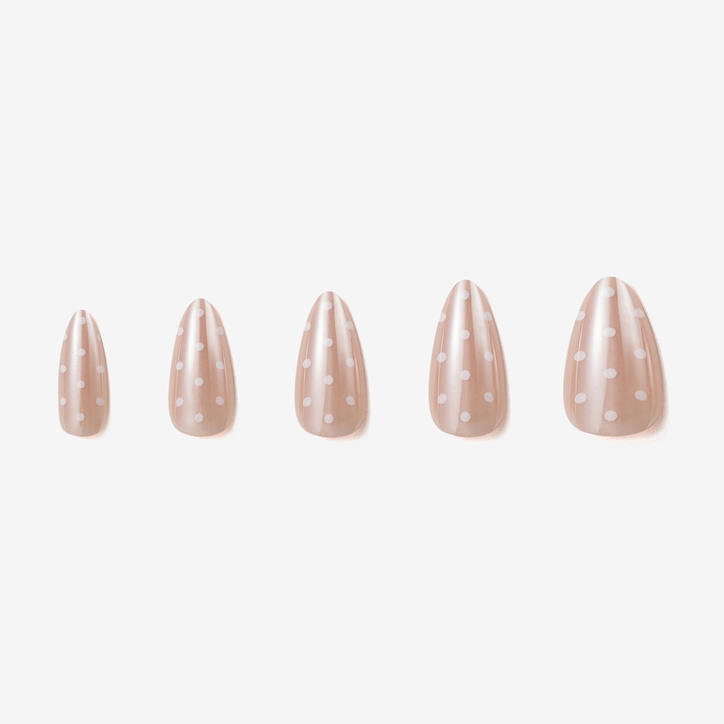 Manucure Chouchette portée sur la main. Teinte beige avec motif à pois blanc. Faux ongles press-on en forme d'amande. Effet brillant naturel. Par SOIMEA Paris